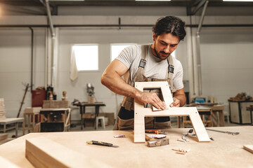 Wall Mural - Young man carpenter wearing uniform working in joinery making wooden furniture