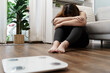 © Charlie's - Sad woman with fat upset bored of dieting Weight loss fail  Fat diet and scale sad asian woman on weight scale at home weight control