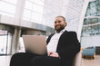 © BullRun - Cheerful businessman sitting with laptop in spacious hall