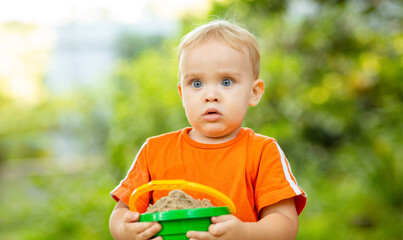 Wall Mural - A little blond boy playing in the sandbox at the playground outdoors. Portarit of toddler with full bucket of sand