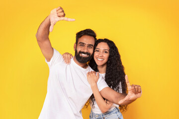 Wall Mural - Cheerful Middle Eastern Couple Framing Themselves For Photo, Yellow Background