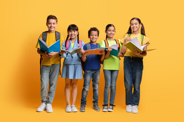  Cute multiethnic schoolchildren with backpacks holding textbooks, yellow background