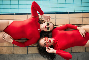 Poster - Sunglasses, swimwear and fashion women or friends in red bodysuit at indoor swimming pool. Portrait above young people relax with sports aesthetic, style and art or luxury in designer clothes