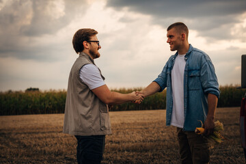 Wall Mural - Side view of two men shaking hands in he fields.