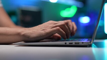 Close-up side view of unrecognizable programmer hacker male working typing on keyboard laptop computer at dark room on blurred background of bokeh neon light. Freelancer using laptop working from home