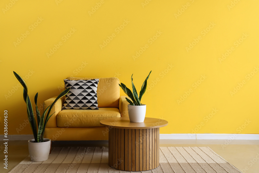 Comfortable armchair, coffee table and houseplants near yellow wall