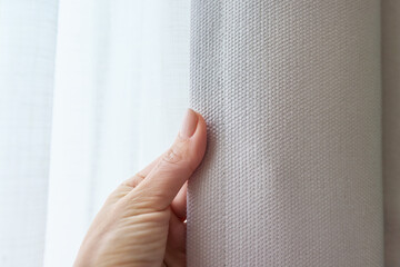 Close-up of hand touching gray curtain on window