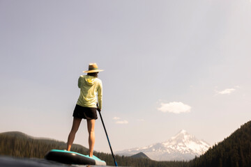 Wall Mural - A young woman cools off in an alpine lake at the base of Mt. Hood with her standup paddle board on a summer day. 