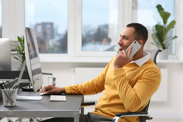 Sticker - Young man talking on smartphone while working with computer at table in office