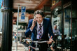 © Marko Geber - Young caucasian businessman talking on his smart phone and hearing good news while commuting to work with his bicycle