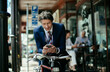 © Marko Geber - Young caucasian businessman using a smart phone while commuting to work with his bicycle