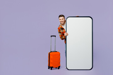 Wall Mural - Traveler man hold suitcase big huge blank screen mobile cell phone isolated on plain pastel purple background. Tourist travel abroad in free spare time rest getaway. Air flight trip journey concept.