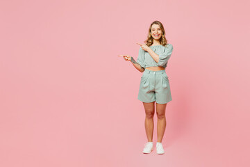 Full body young happy woman she wear casual clothes look camera point index finger aside indicate on workspace area copy space mock up isolated on plain pastel light pink background Lifestyle concept