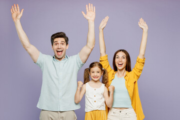 Wall Mural - Young parents mom dad with child kid daughter girl 6 years old wears blue yellow casual clothes do winner gesture clench fists raise up hands isolated on plain purple background. Family day concept.