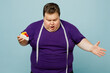 © ViDi Studio - Young confused shocked sad chubby overweight man wearing purple t-shirt casual clothes eat cake show measure tape look at belly isolated on plain pastel light blue cyan background. Lifestyle concept.