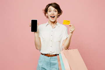 Young woman wear casual clothes hold paper package bags use blank screen mobile cell phone hold credit bank card shopping online isolated on plain pink background. Black Friday sale buy day concept.