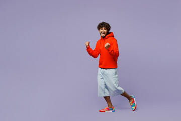 Wall Mural - Full body happy smiling young Indian man wears red orange hoody casual clothes do winner gesture look camera isolated on plain pastel light purple color background studio portrait. Lifestyle concept.