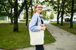 © Shi  - Stylish woman holding white blank canvas tote shopping bag outdoor. Empty reusable canvas tote bag mockup for design. High quality photo