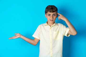 Wall Mural - Beautiful kid boy wearing casual shirt confused and annoyed with open palm showing copy space and pointing finger to forehead. Think about it.