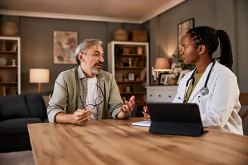 A senior man talking with an African female doctor during a home visit.