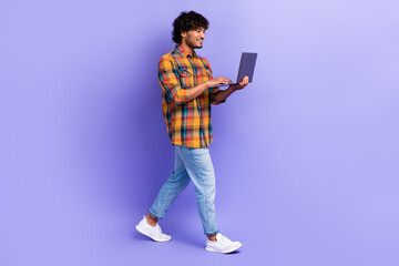 Sticker - Full length profile portrait of positive nice young man walking hold use wireless netbook isolated on purple color background