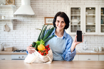 Woman hold bag full fresh vegetables and smartphone for online purchase