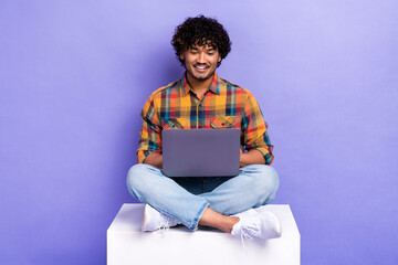 Full body portrait of positive cheerful man sit podium use wireless netbook isolated on purple color background