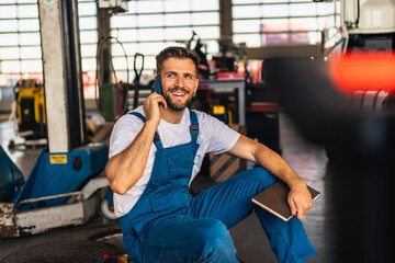 Confident mechanic sitting and talking on a smart phone in a workshop