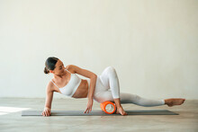 Using foam roller for exercises. Young woman with slim body type is in fitness clothes in the studio