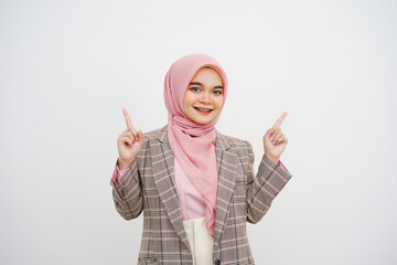 Wall Mural - Studio portrait of beautiful young muslim businesswoman pink hijab smiling at camera pointing her finger at empty space on white background.