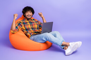 Wall Mural - Full length photo of ecstatic man dressed shirt sit in pouf with laptop raising fists win gambling isolated on purple color background