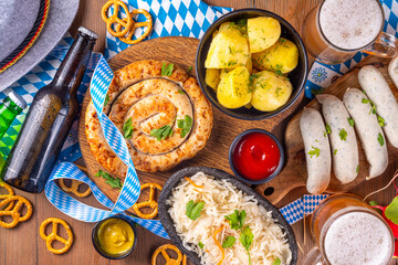 Wall Mural -  Oktoberfest munich traditional festival menu foods - bavarian sausages, pretzels, potato, sauerkraut, beer bottle and mug,  Background flyer for Oktoberfest invitation on old wooden table