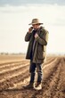 © OMD - shot of a man using his smartphone to make a call while standing on dry farmland