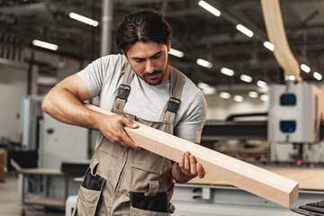 Wall Mural - Young carpenter man looking and choosing wood plank at workshop in carpenter wood factory