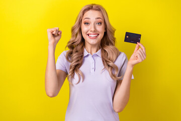 Poster - Photo of delighted overjoyed person hand hold debit card raise fist achievement isolated on yellow color background