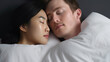 © Sasint - Snoring man. Couple in bed, men snoring and women can not sleep, covering ears with pillow for snore noise. Young interracial couple, Asian woman, Caucasian men sleeping in bed at home.