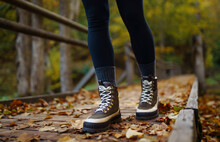 Women's Feet In Boots Go Along A Wooden Walking Path In The Autumn Forest. Vacation Travel Concept, Hiking Trail