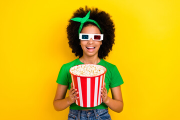 Wall Mural - Photo of funky cheerful girl toothy smile hands hold big popcorn box watch movie 3d glasses isolated on yellow color background