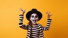 Portrait Of Funny Child In Halloween Disguise Dancing Isolated On Yellow Color Background. Happy Little Girl In Skeleton Costume And Witch Hat, With Skull Makeup Having Fun At Halloween Party