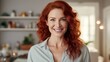 Portrait of smiling mature woman looking at camera with big grin. Successful middle aged woman at home smiling. Beautiful mid adult lady with long red hair enjoying whitening teeth treatment
