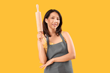 Poster - Young beautiful Asian woman with wooden rolling pin on yellow background