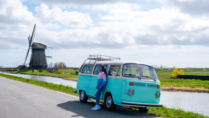 Wall Mural - Asian woman doing a road trip with an old vintage car in the Dutch flower bulb region with tulip fields during Spring in the Netherlands