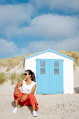 Poster - Asian women visiting the beach of Texel with on the background the white blue house on the beach of Texel Netherlands, a beach hut on the Dutch Island of Texel