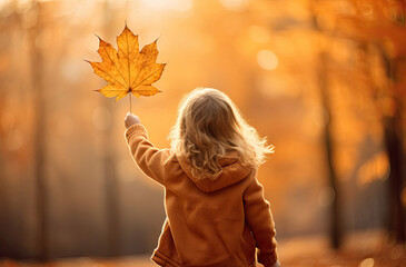 Wall Mural - Back view of a girl holding autumn maple leaf in a park
