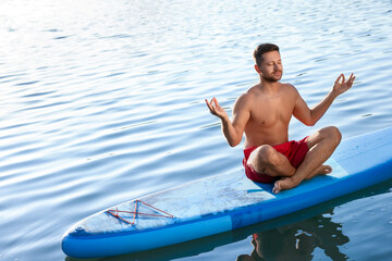 Wall Mural - Man meditating on light blue SUP board on river