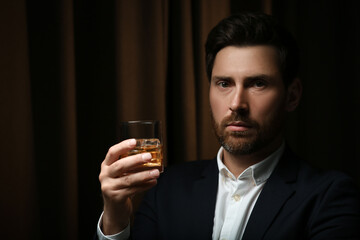 Canvas Print - Man in suit holding glass of whiskey with ice cubes on brown background