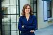 © Nomad Pixel - Portrait of a beautiful young woman with long brown hair, dressed in a blue jacket, standing against the background of an office building. strong and confident business woman