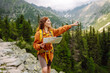 © maxbelchenko - Wanderings. Stylish young woman traveler with a yellow backpack, holds a map, explores hiking trails in the mountains. The concept of travel, vacation.