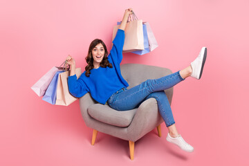 Sticker - Full size portrait of astonished cheerful girl sit comfort chair hold store bags isolated on pink color background