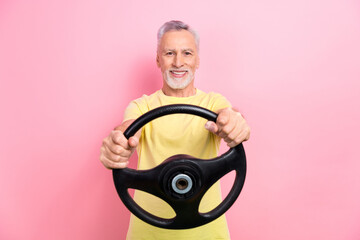 Poster - Photo of satisfied positive man with gray beard dressed yellow t-shirt hold steering wheel test new car isolated on pink color background